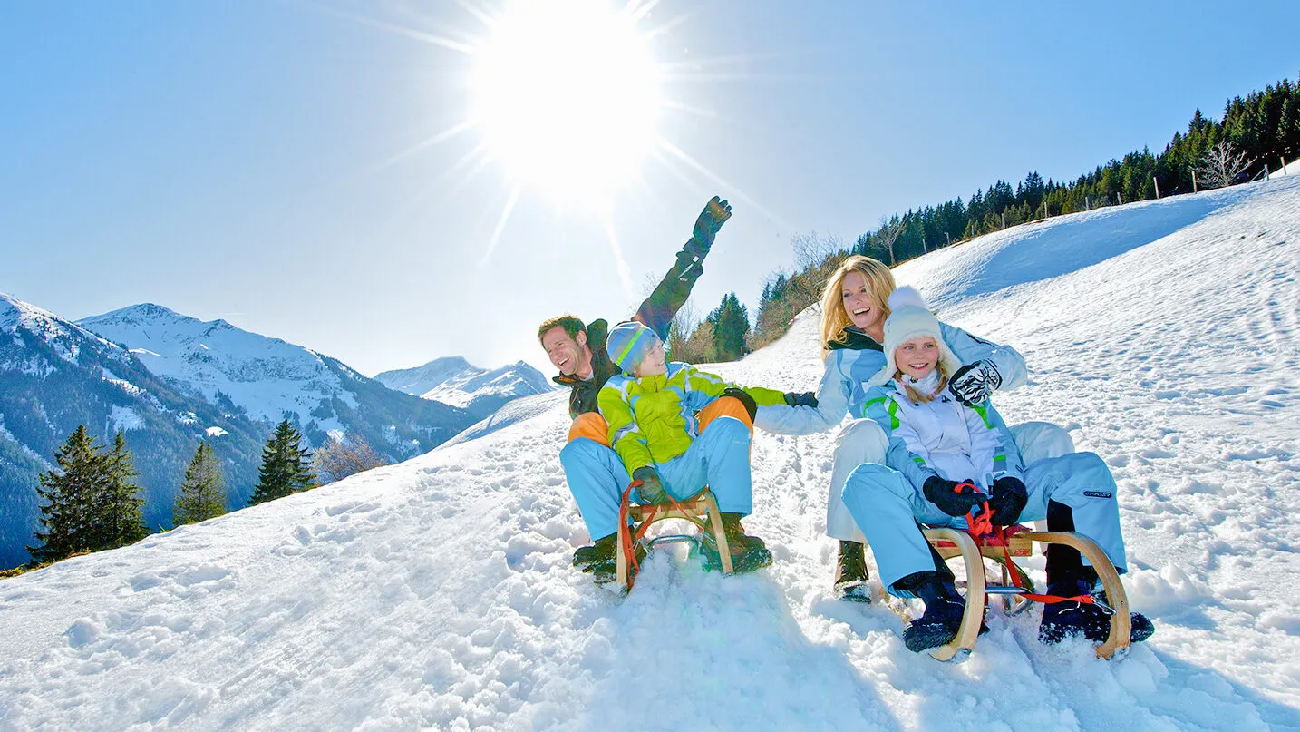 Winterurlaub mit der Familie beim Rodeln in den Alpen